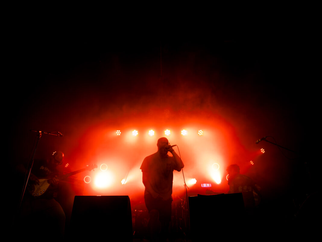 Foto: Goodbye, Old Me in der Sputnikhalle Münster. Der Sänger mittig vor dramatisch rotem Licht, eingerahmt von Bassist und Gitarrist.