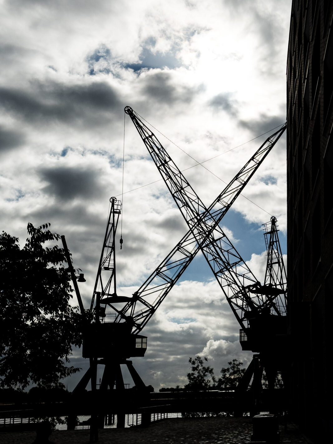 Foto: Kransilhouetten in der HafenCity. Gegens Licht fotografiert sieht man zwei alte Hafenkräne wie man sie sieht, wenn man vorm Edeka steht.