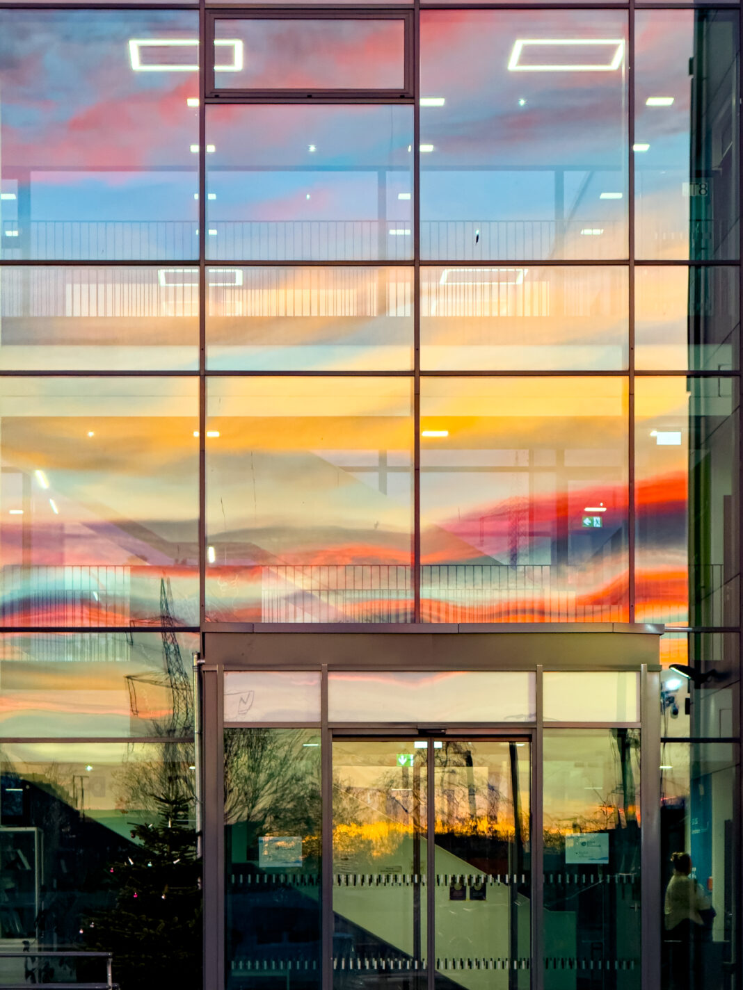 Foto: Abendhimmel im Spiegel. Blick auf eine gläserne Fassade, in der sich der bunte Abendhimmel spiegelt.