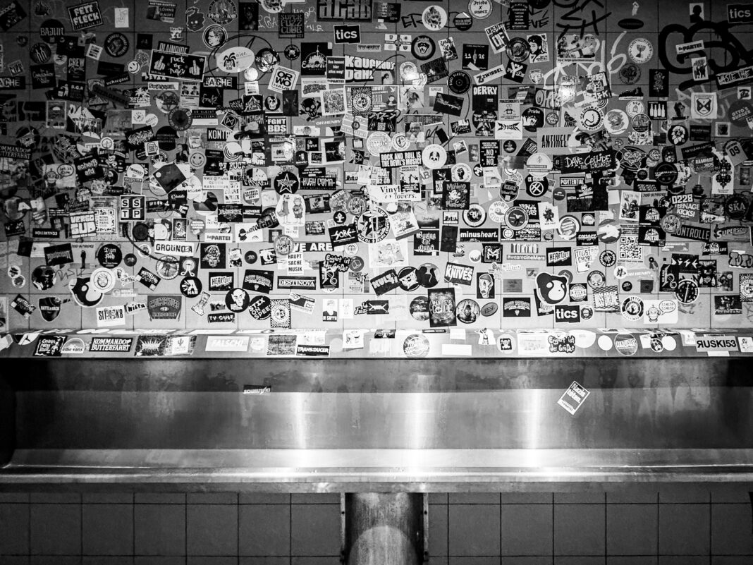 Foto: Die Pissrinne im Gebäude 9. Eine klassische Pissrinne unter einen Wand voller Aufkleber.