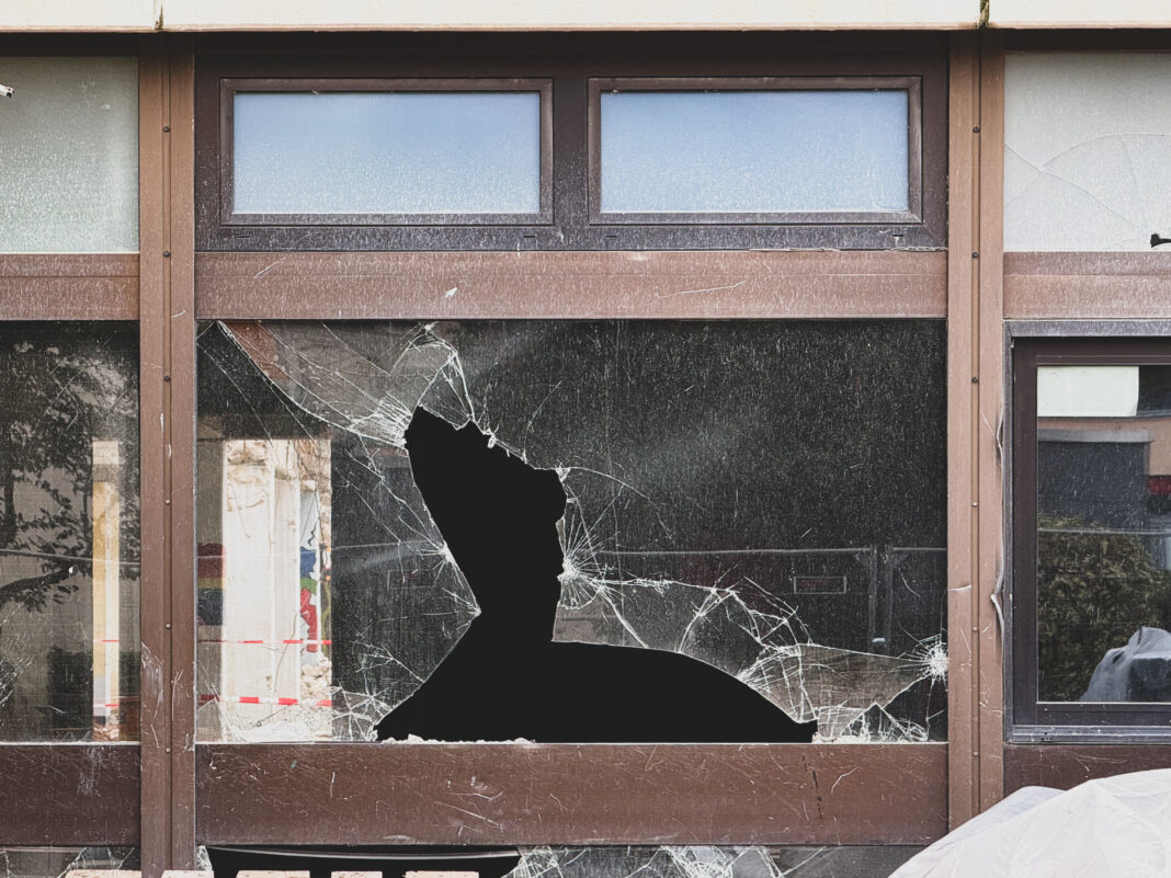 Foto: Kaputtes Fenster. Abriss der alten Gesamtschule. Wir sehen eine zerbrochene Scheibe in einem braunem Fensterrahmen.