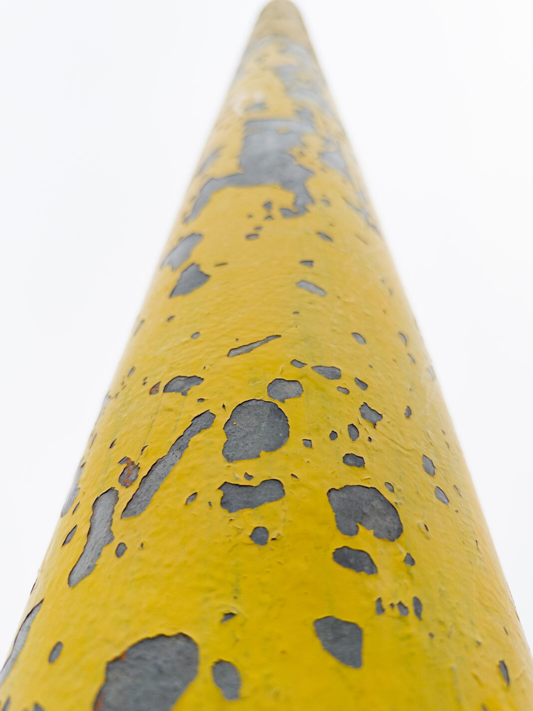 Foto: Ehemals gelber Mast Foto: Ehemals gelber Mast. Der Blick von unten nach oben einen Metallmast entlang, der seine besten Tage hinter sich hat. Der gelbe Lack bröckelt und hat lauter Lücken und Risse.